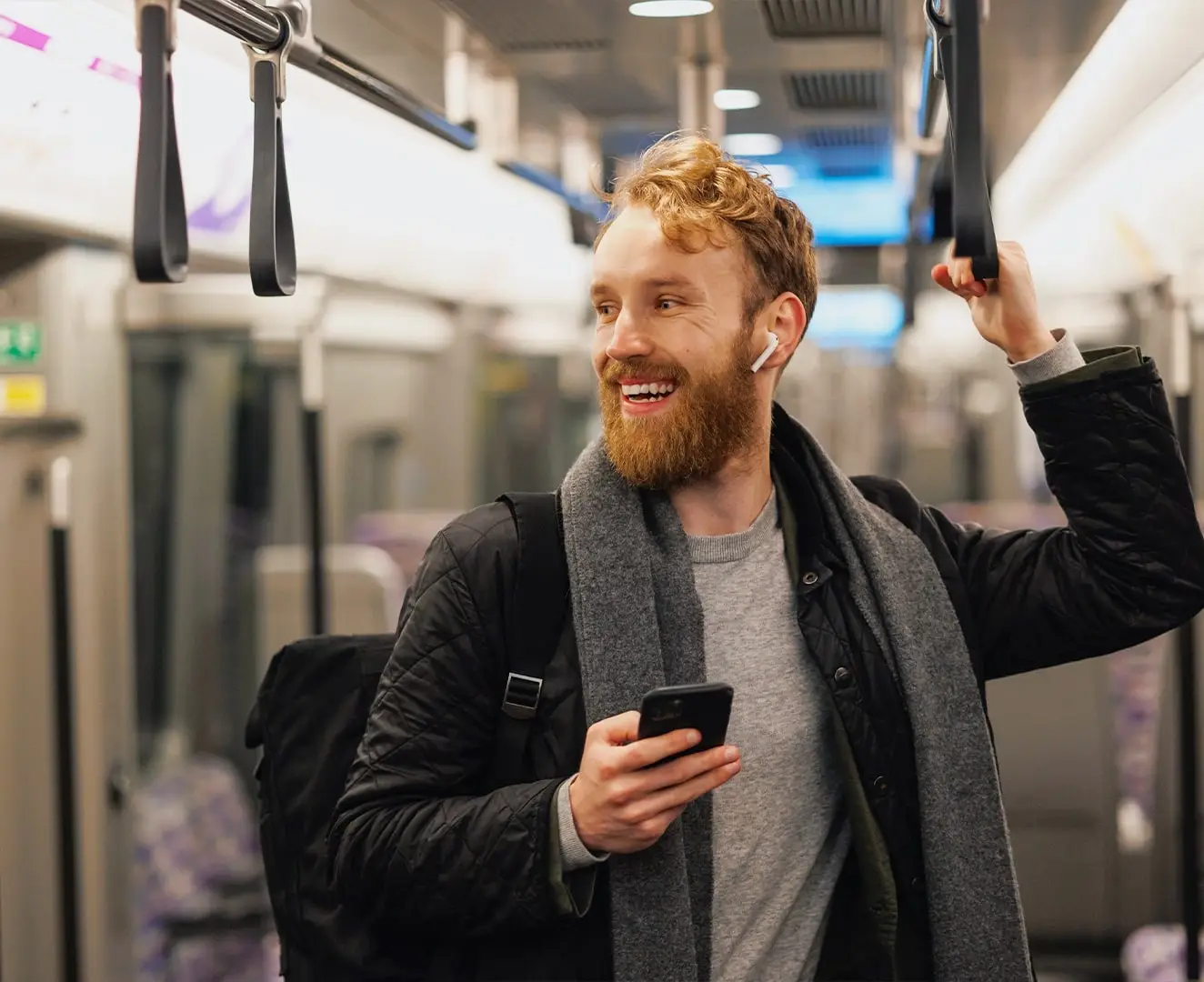 Ein lachender junger Mann fährt gerade mit der U-Bahn zu seinem Marketingjob.